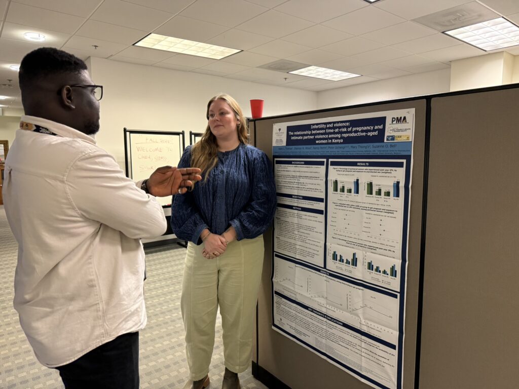 Graduate student presenting a research poster on reproductive health to an attendee during the Annual Graduate Student Networking Event in the CHEA office.