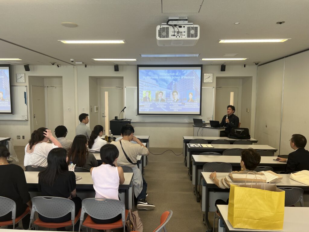 A presenter speaks to an audience in a lecture hall during an orientation slide titled 'Introduction of St. Marianna University School of Medicine'